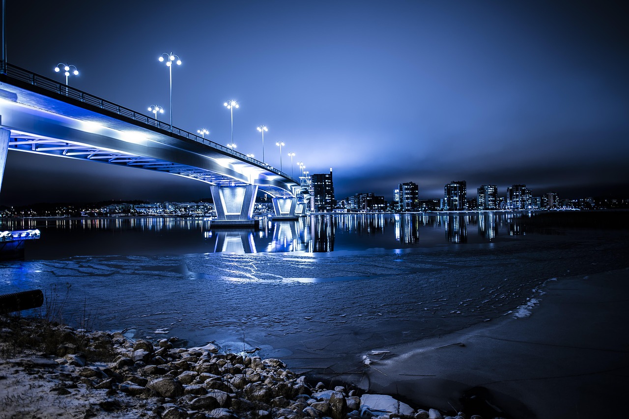 An illuminated bridge connecting a waterfront city at blue hour